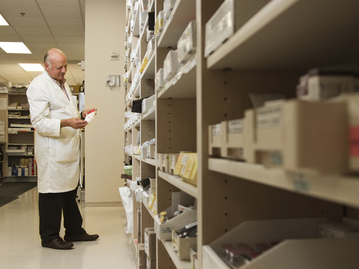 A pharmacist reading a medication label in a pharmacy stockroom aisle